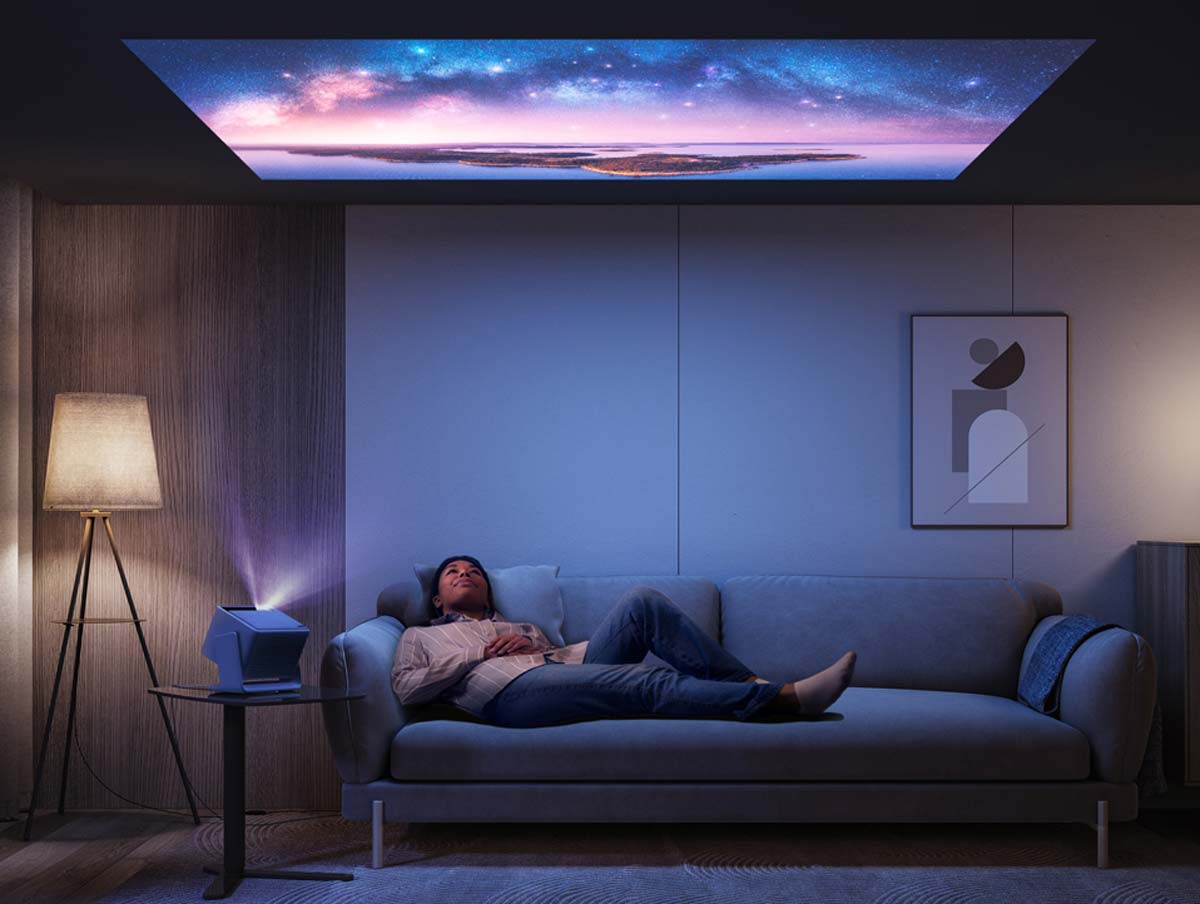 Person auf Sofa, Beamer projiziert Sternenhimmel.