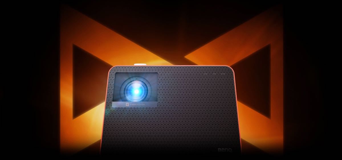 Beamer mit leuchtendem Objektiv vor Hintergrund.