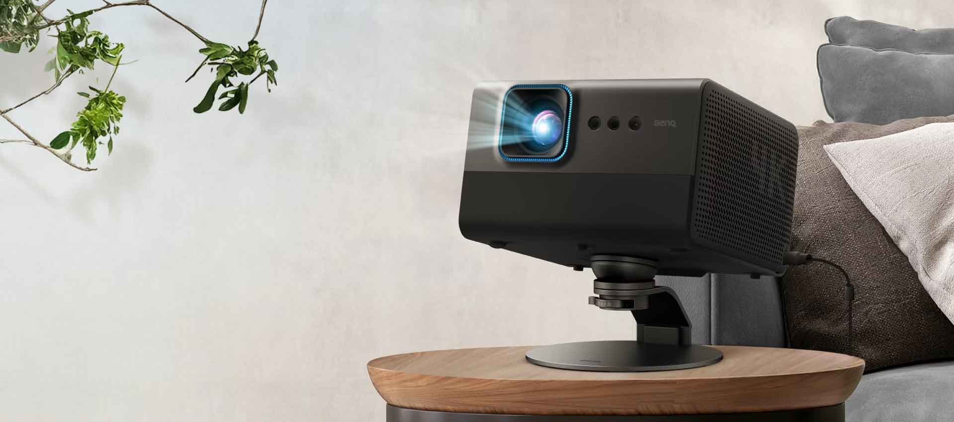 Beamer auf Tisch neben Sofa und Pflanzen.