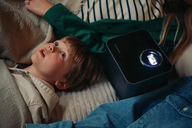 Kind schaut Film mit Beamer im Bett.