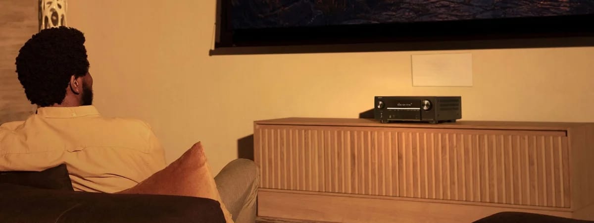 Mann auf dem Sofa im Heimkino, vorn das Sideboard mit dem Verstärker