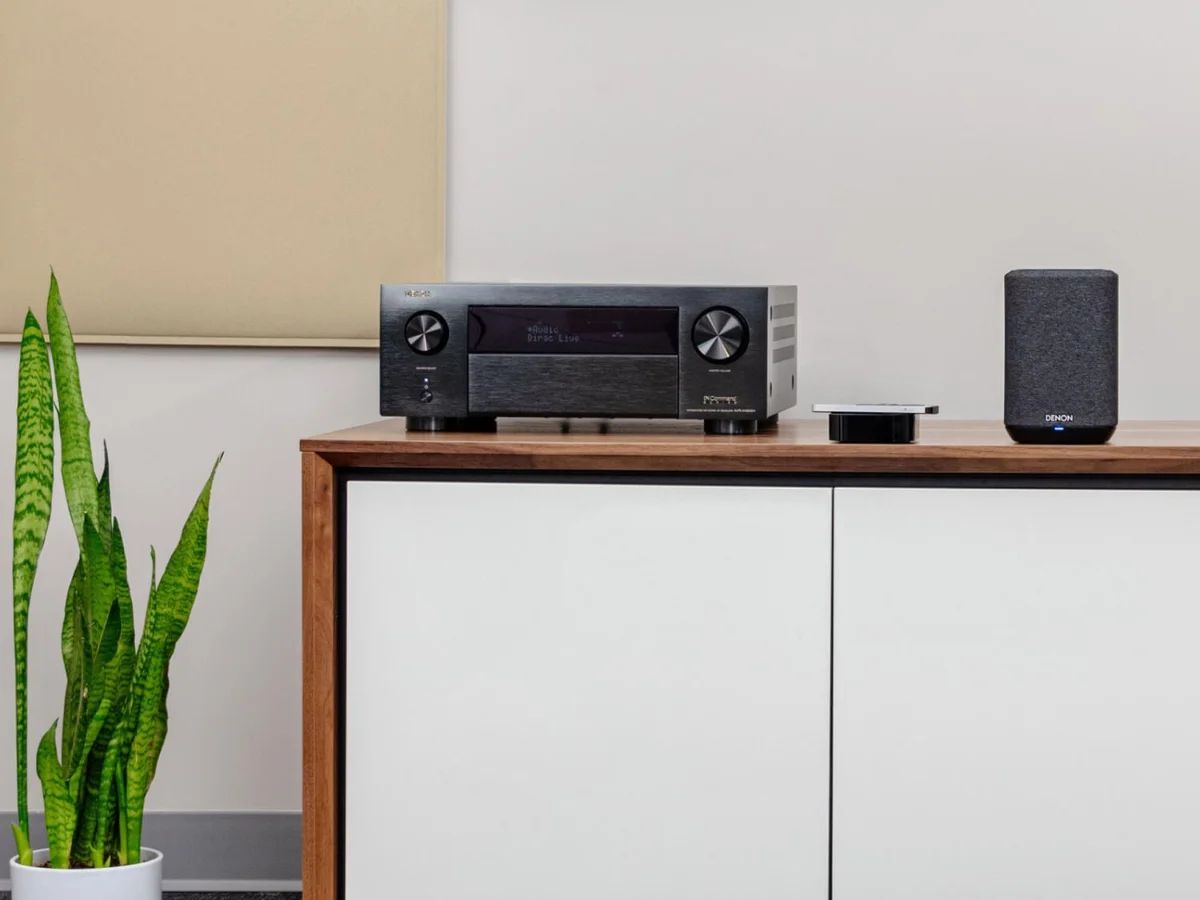 AV-Verstärker auf einem weißen Sideboard, daneben ein Lautsprecher