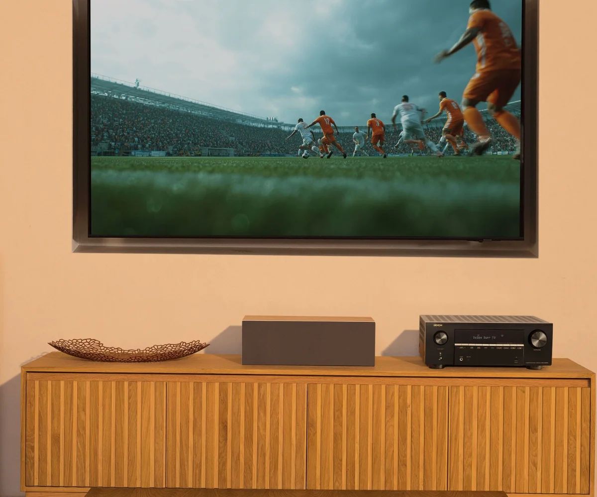 Fernseher an der Wand, darunter der AV-Receiver auf dem Sideboard