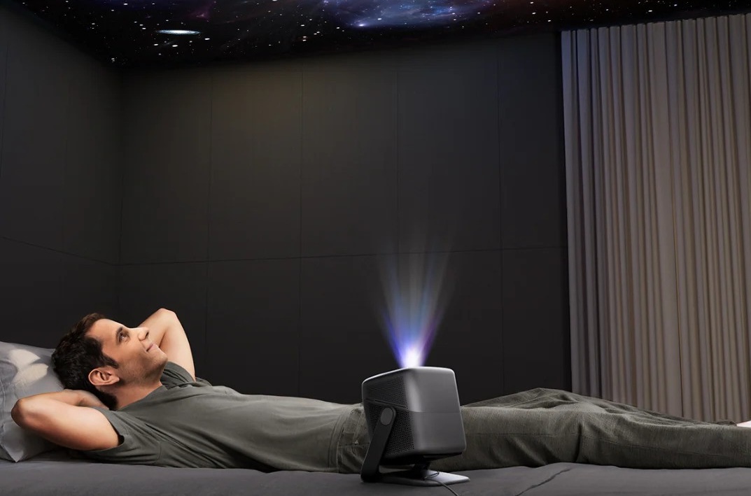 Mann entspannt, Beamer projiziert Sternenhimmel.