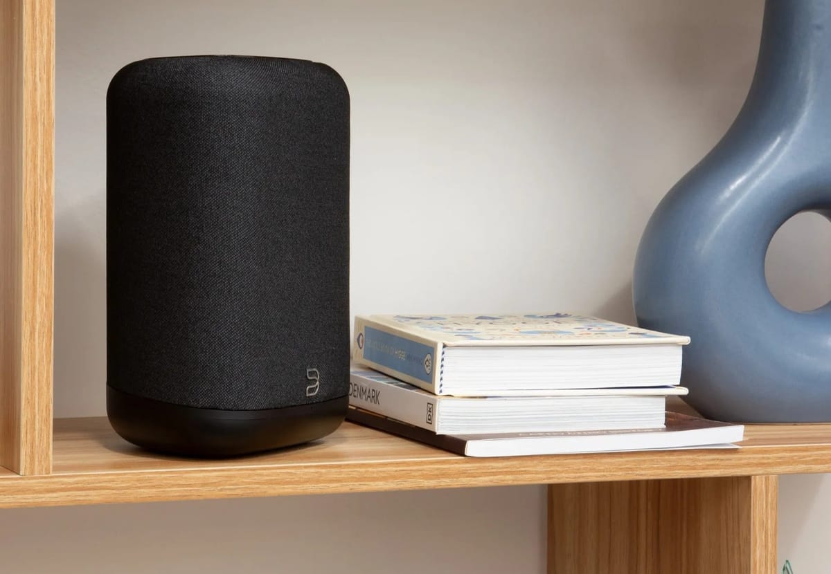 Schwarzer Lautsprecher auf Holzregal neben Büchern.