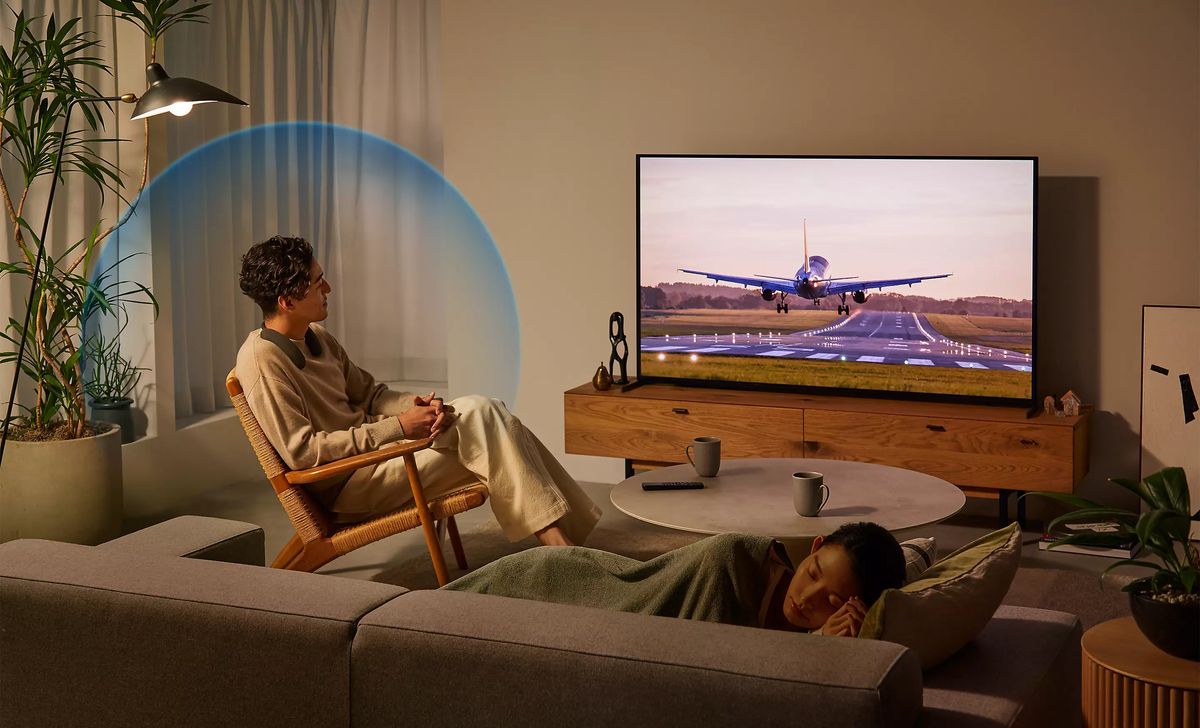 Mann schaut Fernseher, Frau schläft auf Sofa.