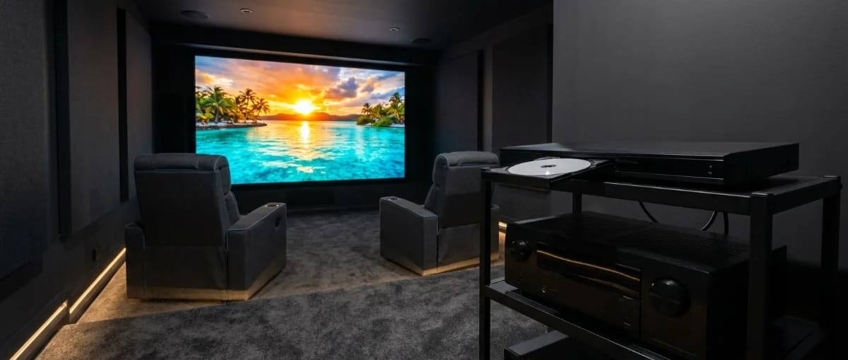 Heimkinoraum mit großer Leinwand und Kinosesseln, im Vordergrund ein Rack mit Disc-Player mit geöffneter Schublade und AV-Receiver