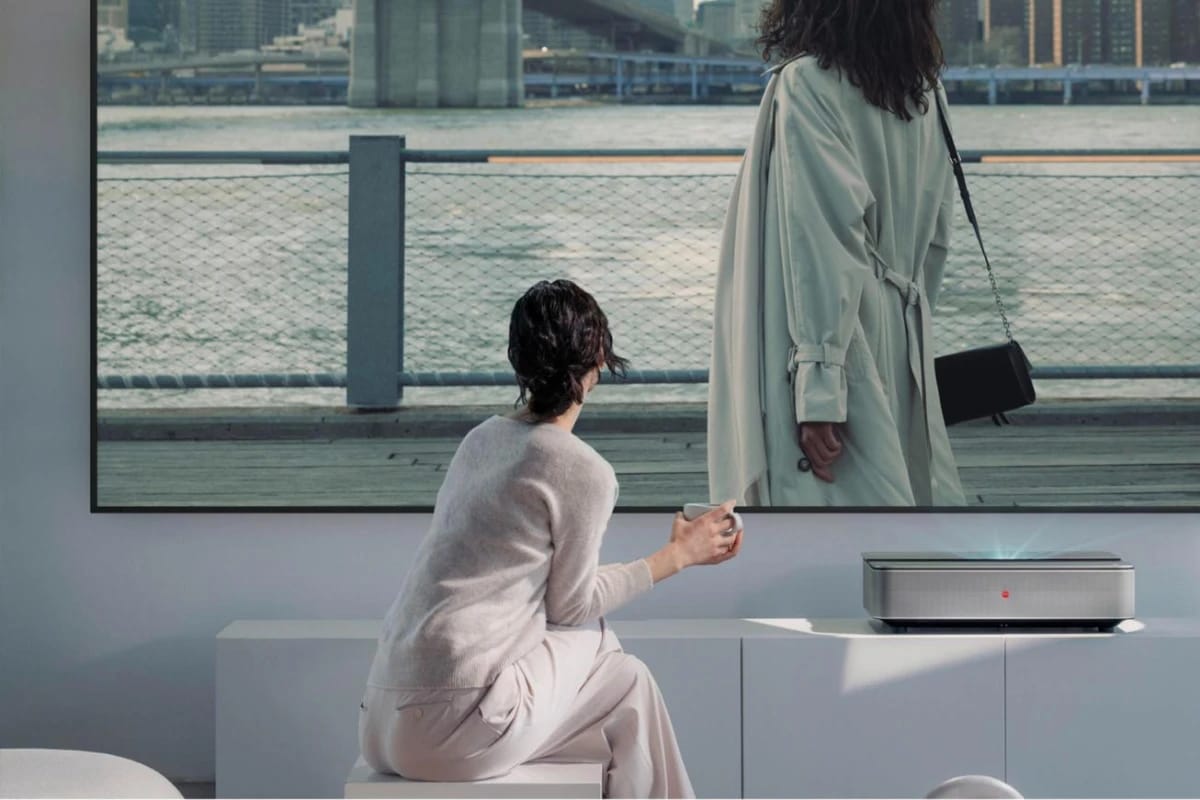 Wohnraum am Wasser, eine Frau sitzt vor dem Sideboard mit dem Laser TV und dem großen Bild