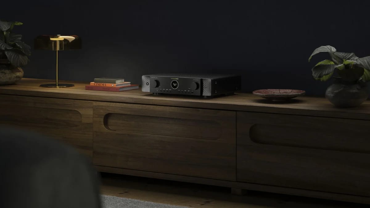 Schwarzer AV-Receiver auf einem langen Holz-Sideboard vor dunkler Wand, daneben Lampe und Pflanze