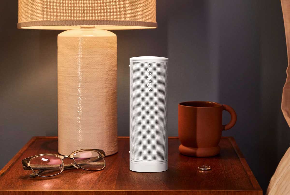 Lautsprecher auf Nachttisch neben Lampe und Tasse.